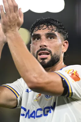 Joueur de l'OM en maillot blanc et bleu avec le numéro visible, levant le bras en célébration lors d'un match. Son visage exprime l'émotion et l'engagement sportif.