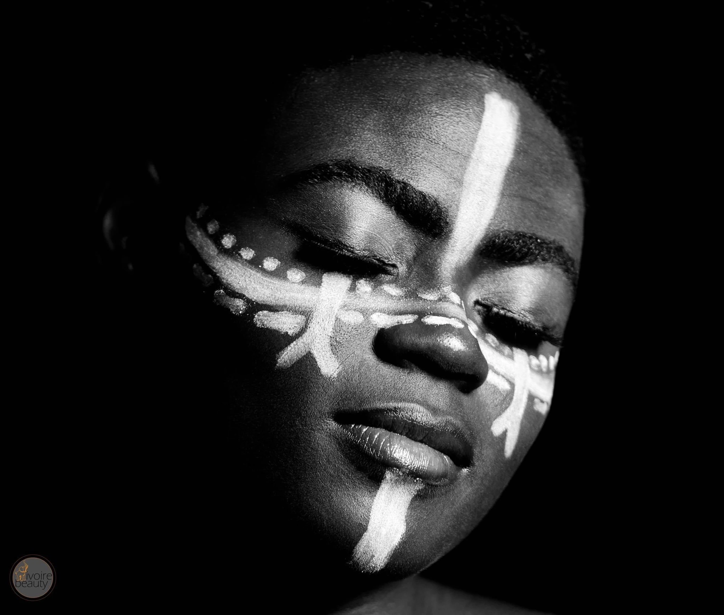 Portrait en noir et blanc d'une personne avec un maquillage artistique géométrique blanc sur le visage, éclairage dramatique sur fond noir, style avant-garde et créatif