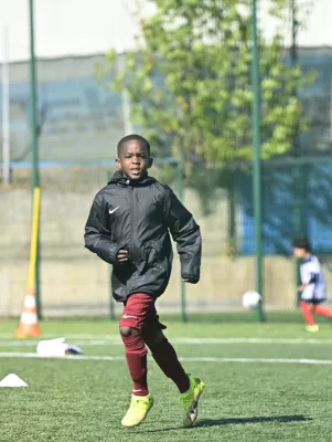 Jeune garçon en tenue de sport Nike courant sur un terrain de football synthétique pendant un entraînement, avec des cônes et d'autres joueurs en arrière-plan