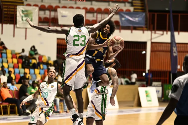 Joueur de basketball en noir effectuant un tir défendu par un adversaire en blanc numéro 23, en salle lors d'un match officiel avec spectateurs